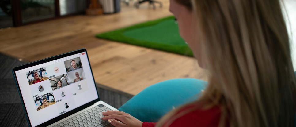 Person sitting on a sofa using a laptop to take part in an online webinar with several participants visible on screen.