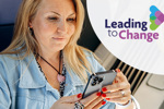 Woman seated on a train using a smartphone, with part of the train interior and a seat visible in the background. The leading to change logo is positioned on the right of the image.