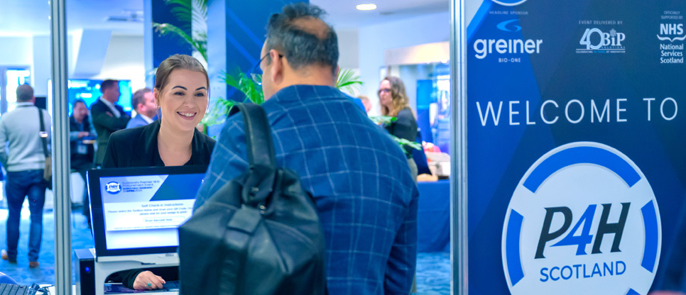 Conference registration area with attendees at a desk and a large blue sign reading ‘WELCOME TO P4H SCOTLAND’, alongside logos for Greiner Bio‑One, 40BiP and NHS National Services Scotland.