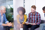 Group of work colleagues in smart casual dress sitting on a sofa against bright background smiling in discussion about an open journal article.