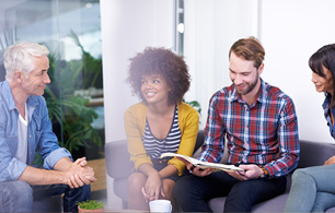 Group of work colleagues in smart casual dress sitting on a sofa against bright background smiling in discussion about an open journal article.