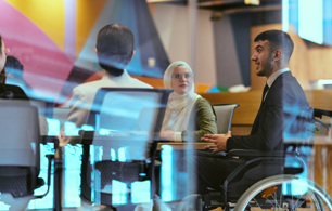People seated around a meeting table in a modern office, including a wheelchair user, engaged in discussion.