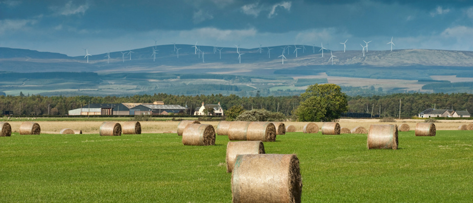 A view of rural Scotland with hay bales and hills in the distance