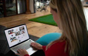 Person sitting on a sofa using a laptop to take part in an online webinar with several participants visible on screen.