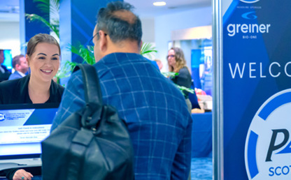 Conference registration area with attendees at a desk and a large blue sign reading ‘WELCOME TO P4H SCOTLAND’, alongside logos for Greiner Bio‑One, 40BiP and NHS National Services Scotland.